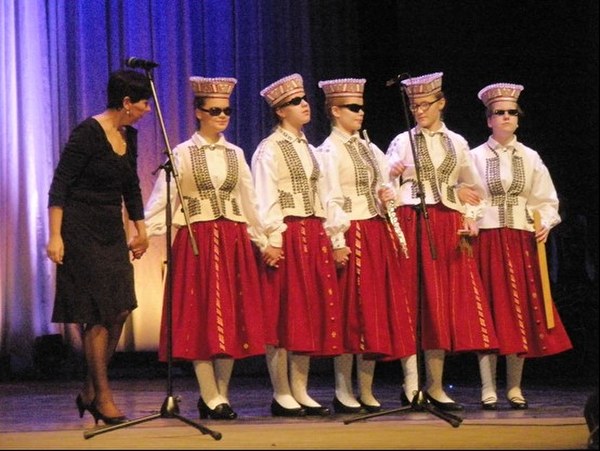 Skolas meitenes taustastērpos uz skatuves kopā ar skolotāju Irēnu Ozoliņu.