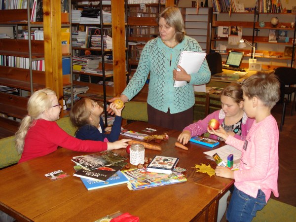 Bibliotēkā bērni pie galda ar bibliotekāri.