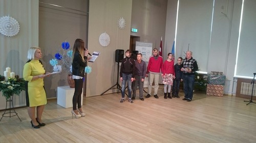 Mūsu skolas bērni lielā zālē priekšā, pasākuma vadītājas ar viņiem runā mikrofonā