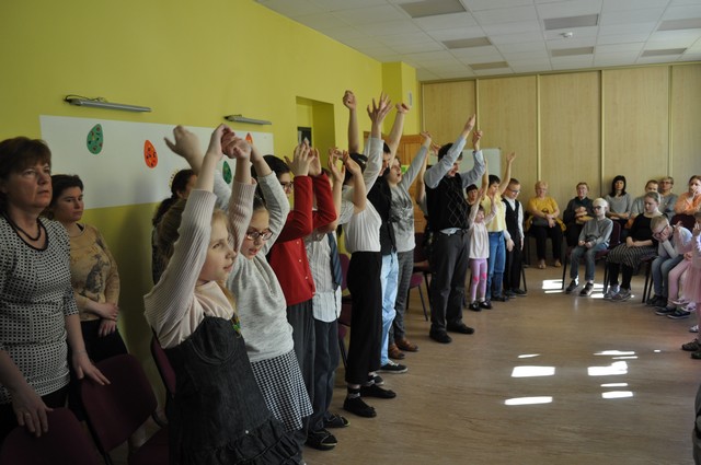 Bērni aplī konferenču zālē paceltām rokām.