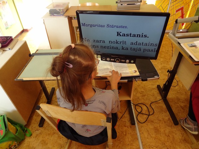 Meitene lasas tekstu par kastaņiem ar palielinošo lasāmo aparātu.
