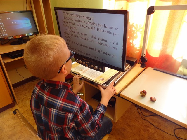 Zēns lasa tekstu ar palielinošo lasāmo aparātu.