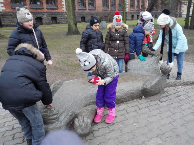Bērni aptausta lielu lauvas figūru muzeja pagalmā.