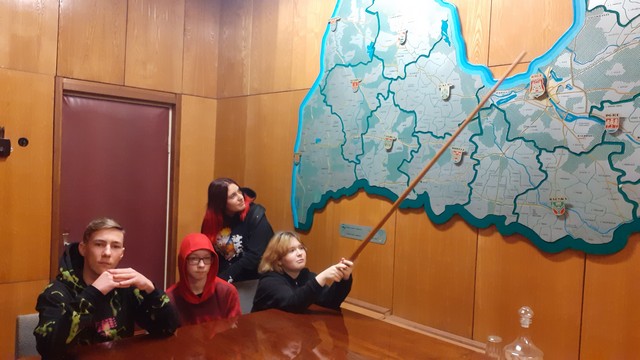 Četri skolēni pie Latvijas kartes. Meitene ar norāda uz kādu vietu kartē.