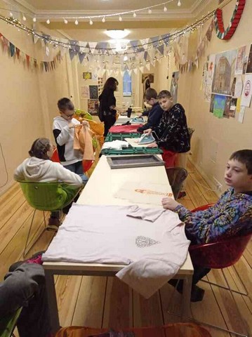 Garš galds, pie kura darbojas skolēni a audumu.