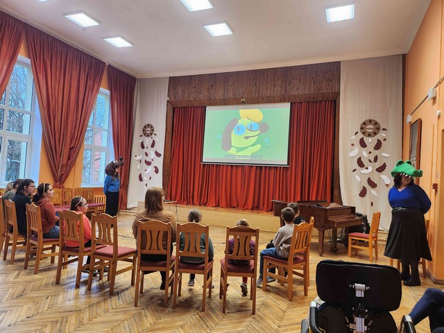 Uz projektora ekrāna tiek rādīts suns Funs, skolēni sēž pretī pusaplī.