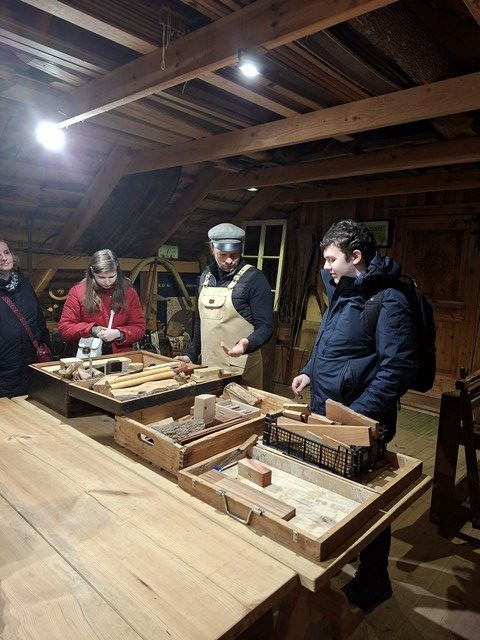 Skolēni koka darbnīcā pie dažādiem koka materiāliem.