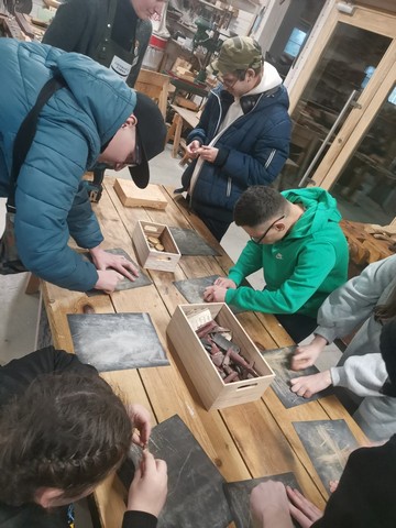 Skolēni kaut ko zīmē uz tumšām koka plāksnēm.