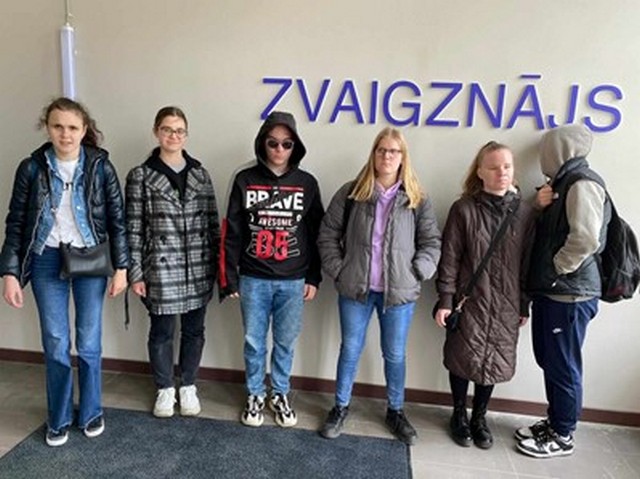 Skolēni pie sienas, uz kuras lieliem burtiem rakstīts "Zvaigznājs"