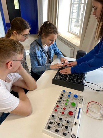 Viena skolniece tausta tastatūrai līdzīgu iekārtu, blakus divi citi skatās.