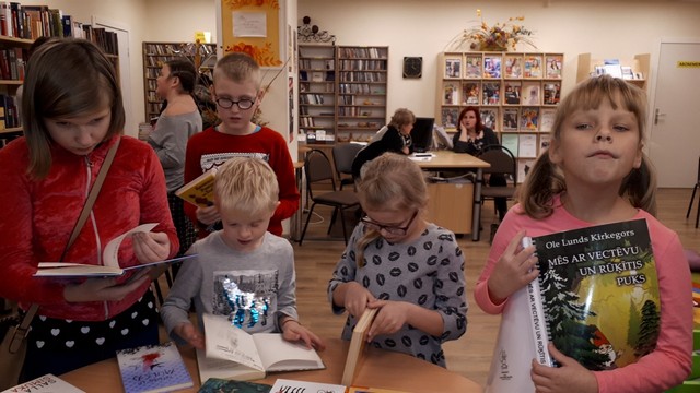 Bērni bibliotēkā pie galda šķirsta grāmatas