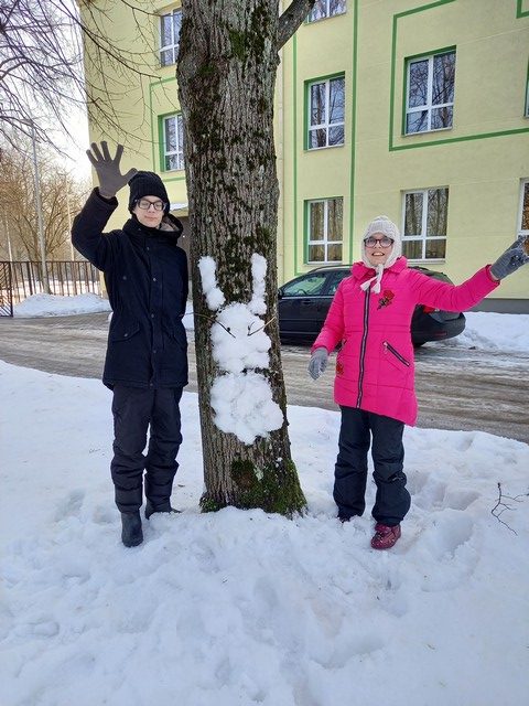 Bērni pie koka ar uzlipinātu zaķi sūta sveicienus