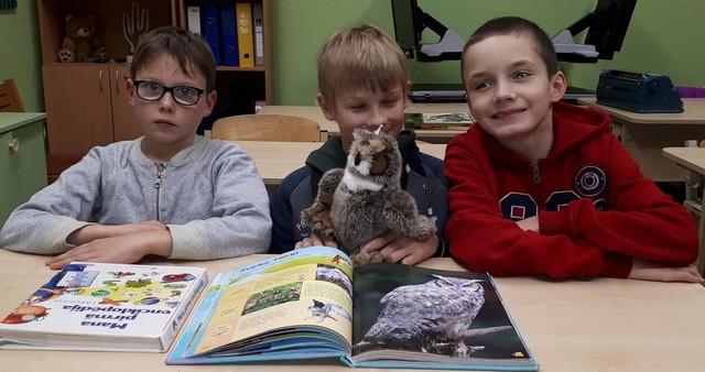 Trīs skolēni sēž solā priekšā grāmata un pūce.