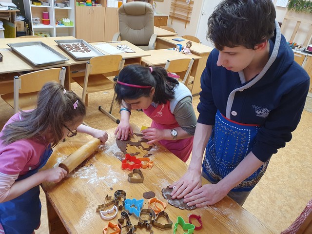 Trīs skolēni rullē, mīca un veido ar formiņām piparkūku mīklu