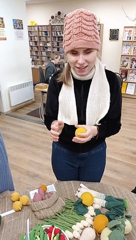 Meitene cepurē ar adītu apelsīnu rokā