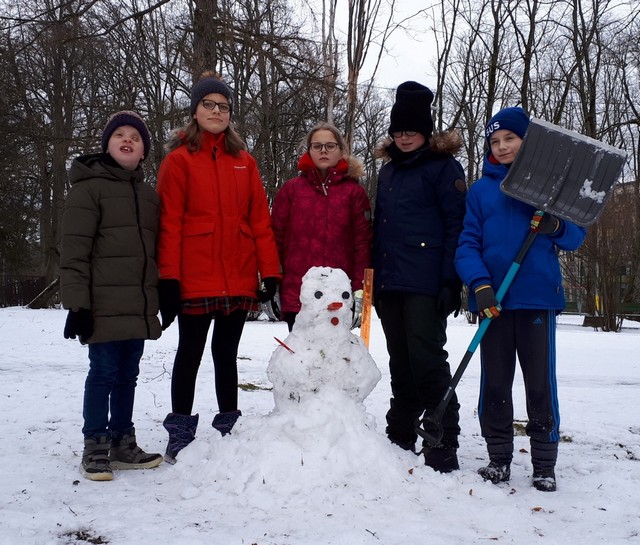 Pieci skolēni pie uzbūvētā sniegavīra.