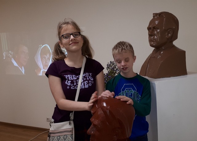 Alberts un Marta stāv, rokas uzlikuši skulptūras galvai.