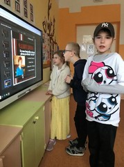 Skolēni pie interaktīvā ekrāna skatās filmu par Latviju.
