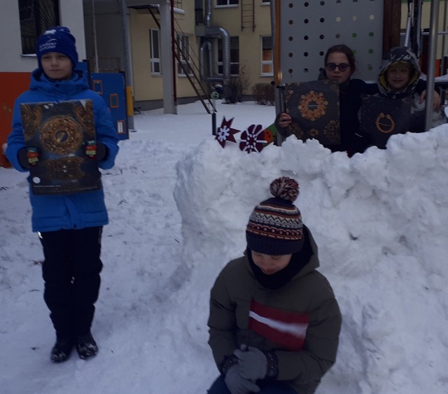 Skolēni pie sniega cietokšna ar latvijas simboliem.