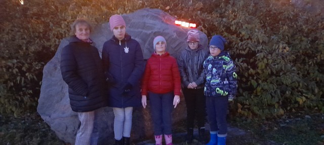 Viena skolotāja un četri skolēni pie liela piemiņas akmeņa.