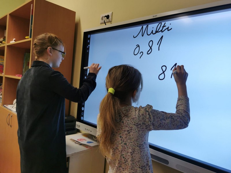 Divas skolnieces uz interaktīvā ekrāna rēķina cenu miltiem.