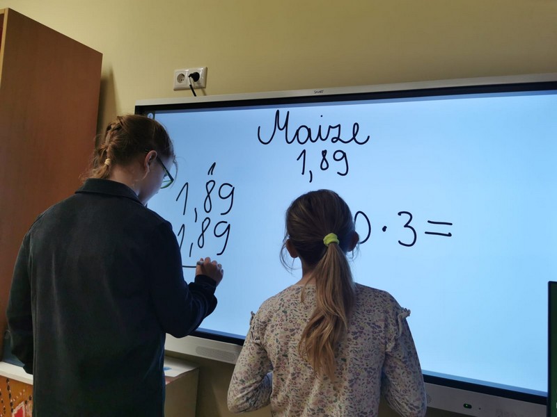 Divas skolnieces uz interaktīvā ekrāna rēķina cenu maizei.