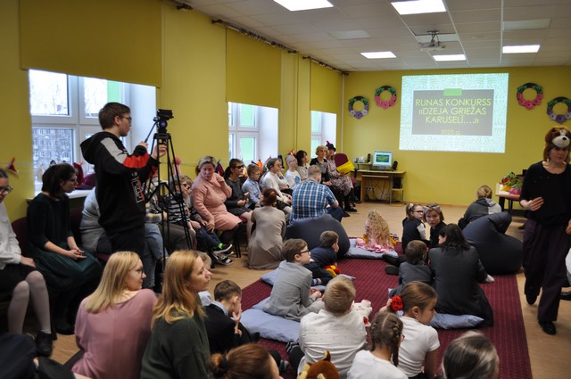 Skolas Konferenču zālē pulcējušies dalībnieki un skolotājas.