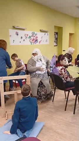 Centrā vecmāmiņa, apkārt skolēni un skolotājas.