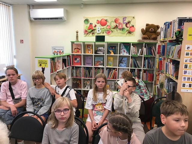 Skolēni sēž divās rindās un klausās stāstījumu.