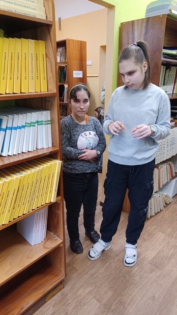 Divas meitenes iet no vienas bibliotēkas telpas uz citu.