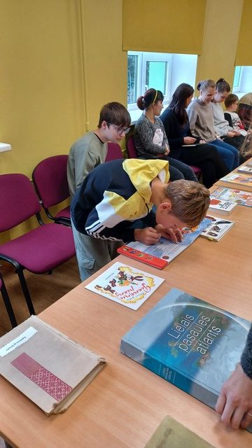 Skolēni apskata grāmatas, kas saliktas uz galdiem Konferenču zālē.