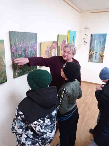 Skolotāja Gundega rāda gleznas, kas ir pie sienas.