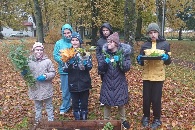 Pieci skolēni skolas parkā tur rokās rudens veltes un rudens lapas.
