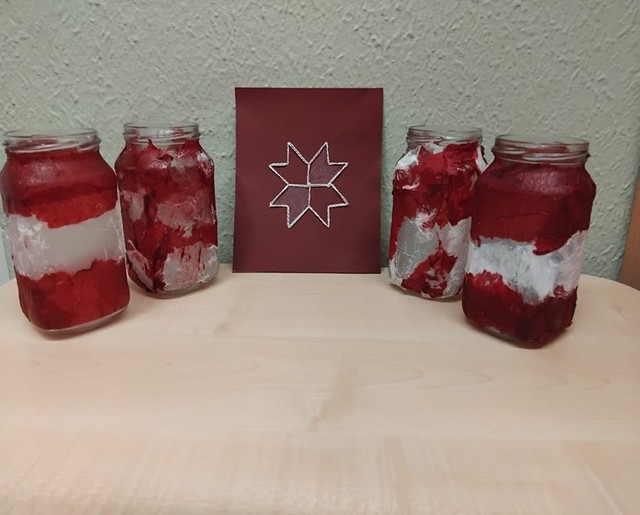 Četras sarkanbaltsarkani nokrāsotas burkas un pa vidu zīmējums.