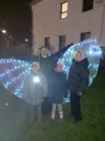 Četras skolnieces stāv pagalmā, vienai lieli spīdīgi spārni kā taurenim.