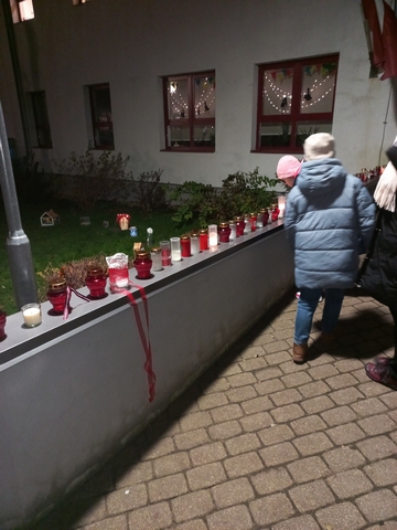 Pie kādas mājas siena ar traukiem ar baltām un sarkanām svecēm.