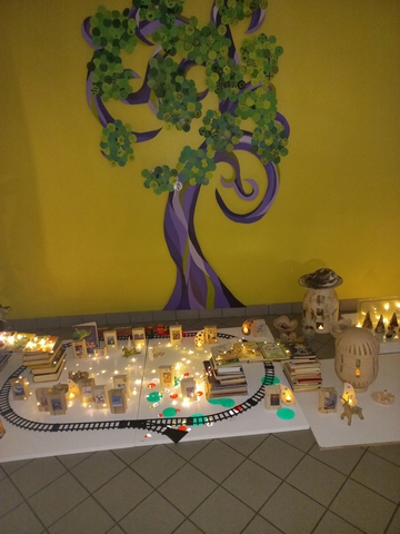 Uz galda izgaismotas spēļu mājas ap kurām spēļu dzelzceļa sliedes.