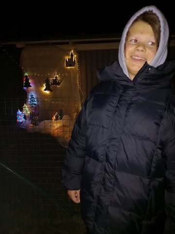 Meitene pie sienas ar mazām izgaismotām eglītēm.