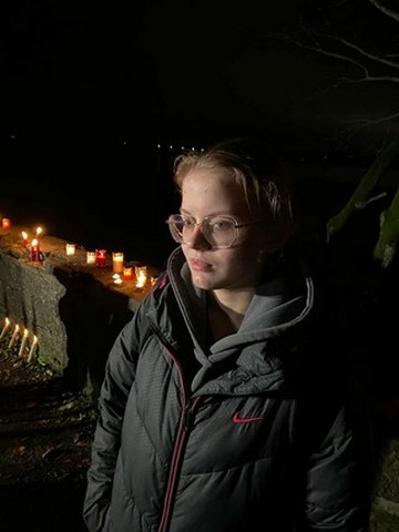 Milēna stāv pie mūra ar svecītēm.