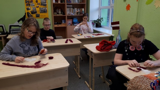 Četri skolēni pie galda veido rotājumus no sarkana auduma.