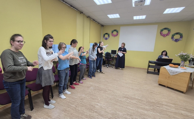 Skolēni rindā piecēlušies kājās un ar rokām veido kaut kādas kustības.