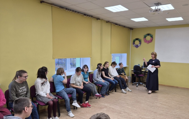 Skolēni sēž rindā uz krēsliem, skolotāja Inese kaut ko viņiem stāsta.