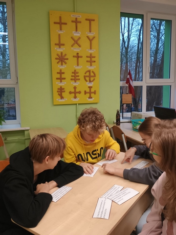 Skolēni pie galda lasa lapiņas.