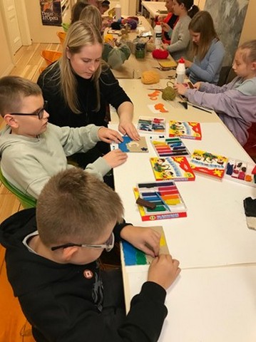 Solēni radošās darbnīcās veido ar plastilīnu, muzeja dariniece palīdz zēnam.