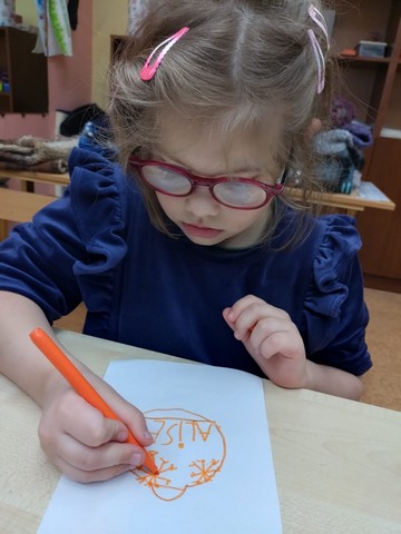 Meitene zīmē ar oranžu flomasteru.