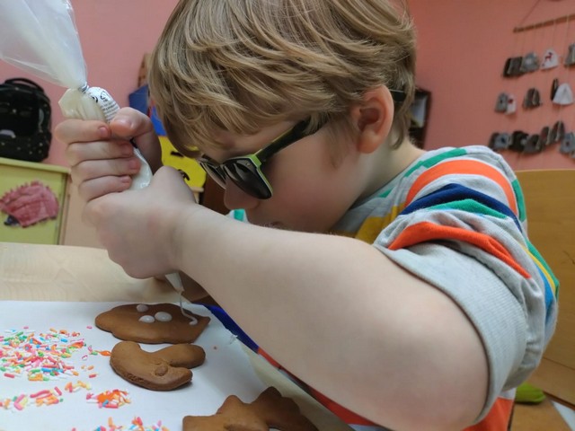 Zēns tumšās brillēs spiež baltu glazūru uz piparkūkām.