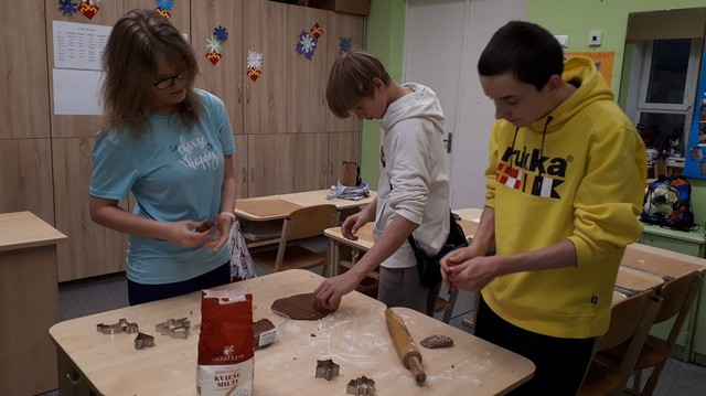 Divi zēni un viena meitene uz galda veido piparkūkas.