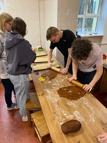 Divi zēni rullē mīklu, divas metenes palīdz.