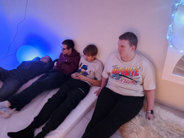 Četri skolēni Baltajā istabā atlaidušies uz matrača un segas.