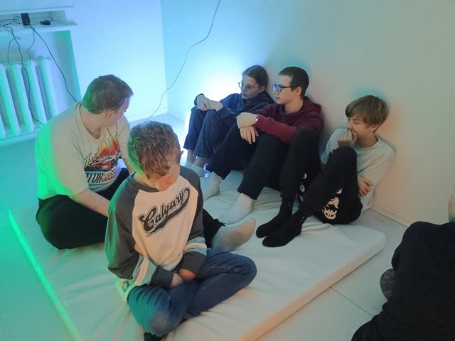 Pieci skolēni sēž uz matrača un klausās.